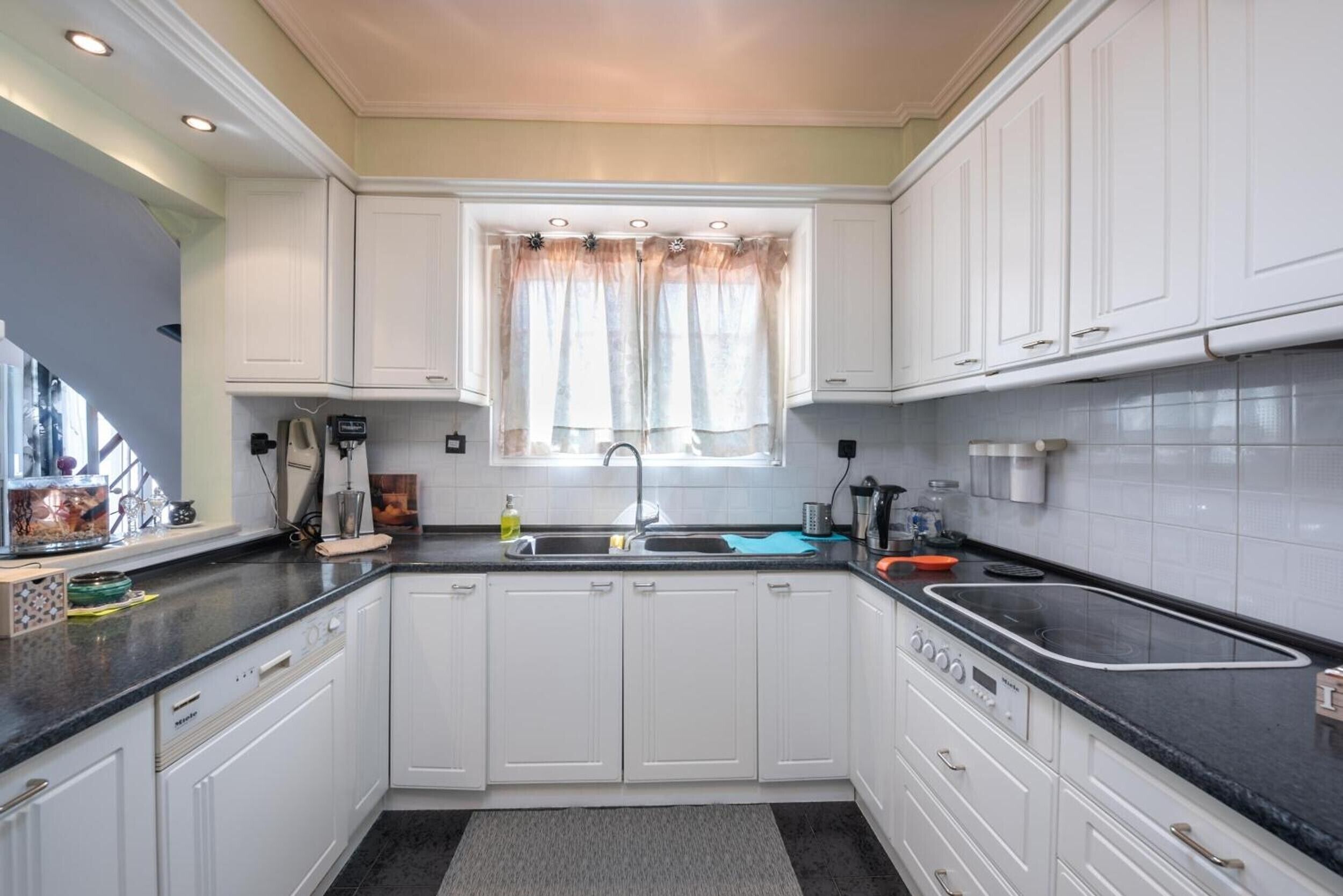 A kitchen with white cabinets, a black countertop, a window with curtains, and a sink.