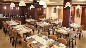 Un comedor de hotel con varias mesas, sillas e iluminación colgante.