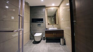 Un baño moderno con cabina de ducha de vidrio, un inodoro, un lavamanos con espejo y un cubo de basura.