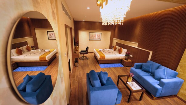 Habitación de hotel con dos camas, un sofá, una silla, una mesita y un espejo.