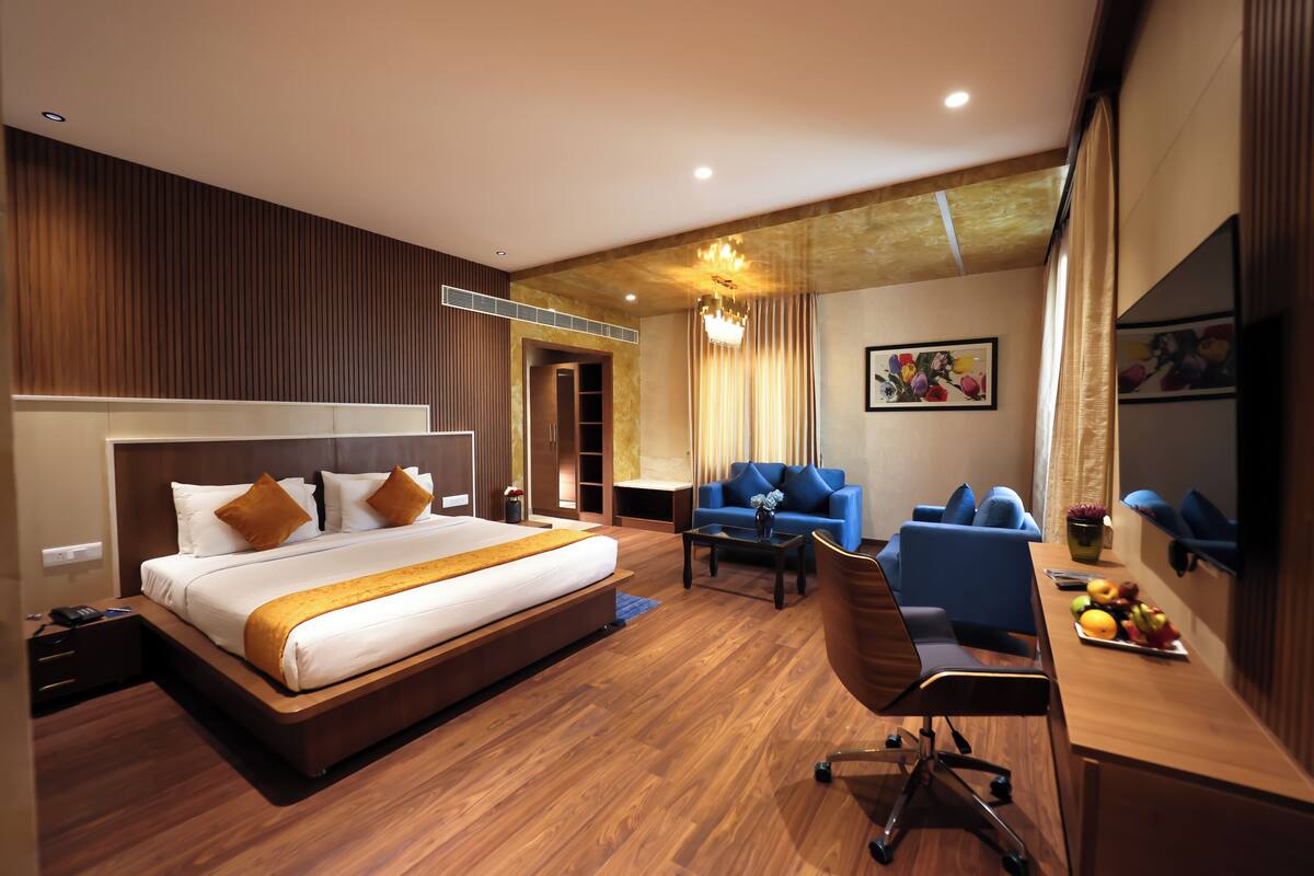 A modern hotel room with a large bed, a desk with a chair, a sofa, and a TV.