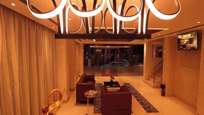 Un moderno vestíbulo de hotel con un conjunto de sofás, una mesa de centro, una escultura decorativa y un televisor montado en la pared.
