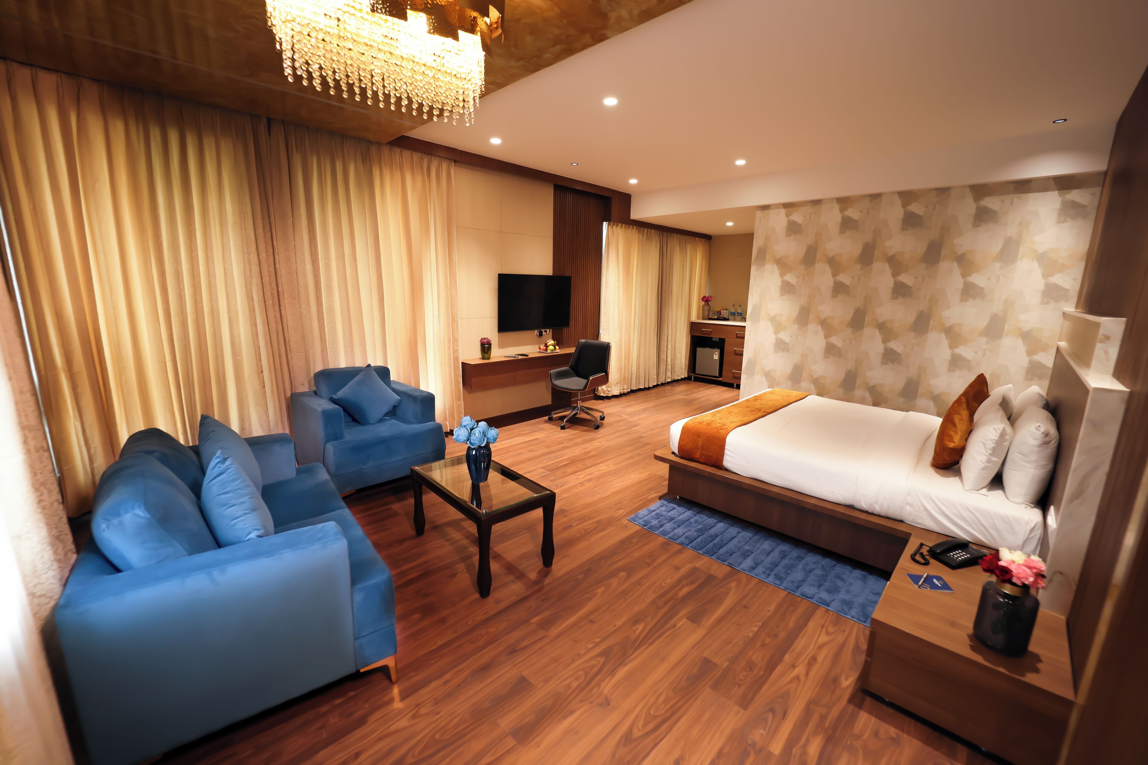 A hotel room with a sofa, a bed, a desk, a TV, and a chandelier.