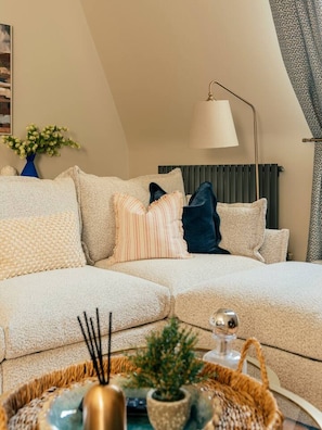 Un salon chaleureux avec un canapé d’angle, une lampe sur pied, un radiateur et un vase décoratif.