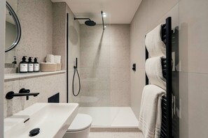 A modern bathroom with a shower, toilet, and sink, featuring a towel rack and toiletries. - Stunning Central Apartment with Sky Light Views (North Yorkshire)