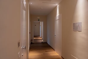 Corredor de hotel com piso de madeira, paredes brancas e portas em ambos os lados.