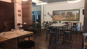 A restaurant interior with multiple tables and chairs, a large painting on the wall, and a bar area. - B&B Corte mopps (Grottaglie)