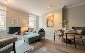 Ein modernes Wohnzimmer mit einer Couch, einem Esstisch mit Stühlen, einem Heizkörper und einem Fenster mit Vorhängen.