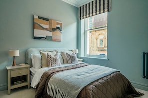 Ein Schlafzimmer mit einem Bett, zwei Nachttischen, einem Fenster mit Ausblick und einem Wandbild.