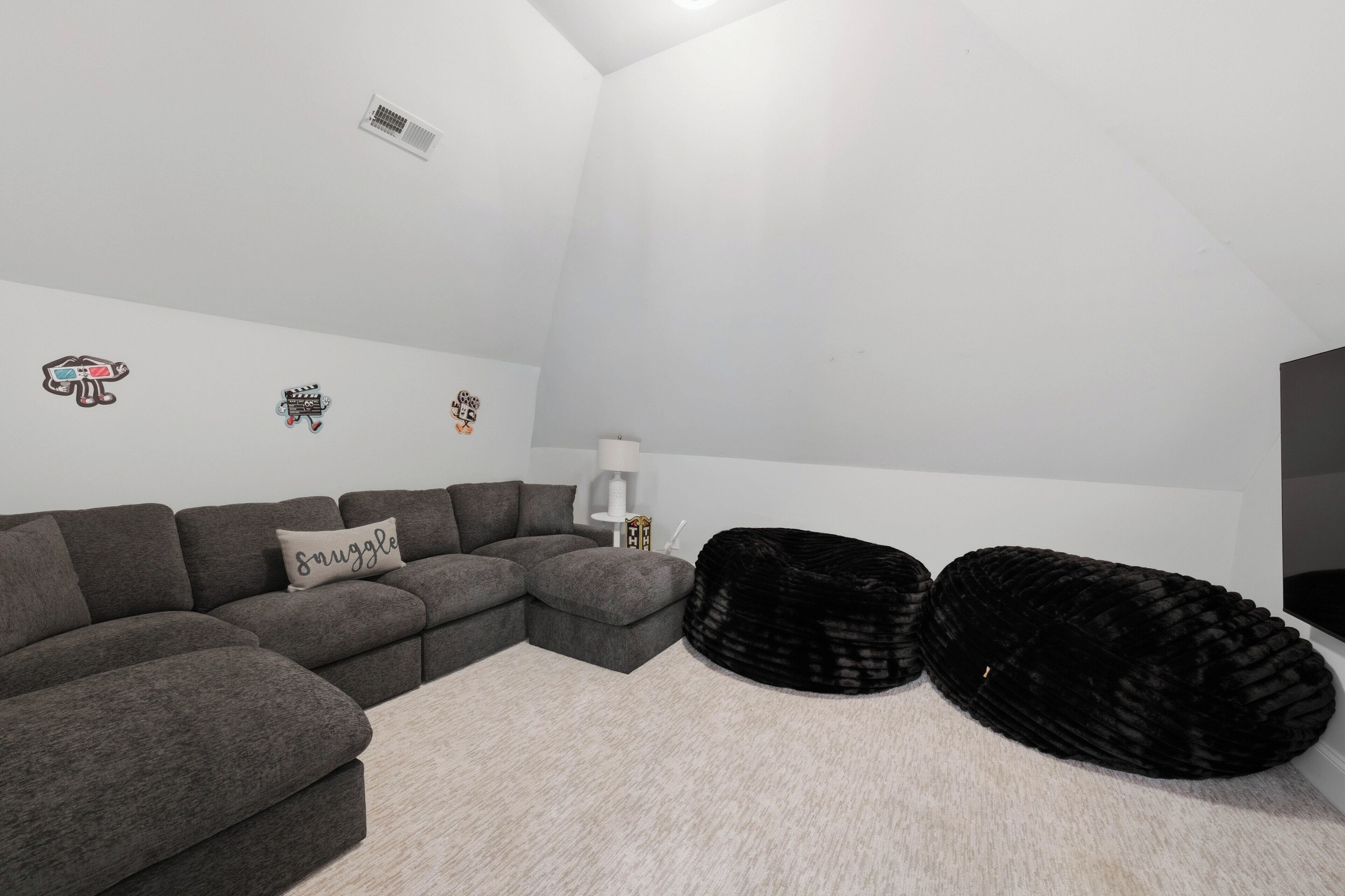 A modern living room with a sectional sofa, black bean bag chairs, a small table, and wall decorations.