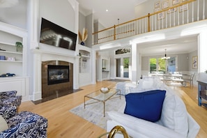 A spacious living room with a fireplace, a dining area, and a staircase leading to an upper level. - Lakefront + Private Dock + Hot Tub + Fire Pit + Game Room | Belle Pines Hideaway (Lake Norman of Catawba)