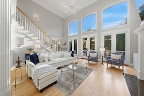 A spacious living room with a white staircase, a large window, and a balcony. - Lakefront + Private Dock + Hot Tub + Fire Pit + Game Room | Belle Pines Hideaway (Lake Norman of Catawba)