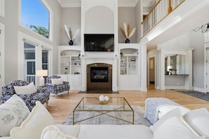 A spacious living room with a fireplace, high ceilings, and a staircase.