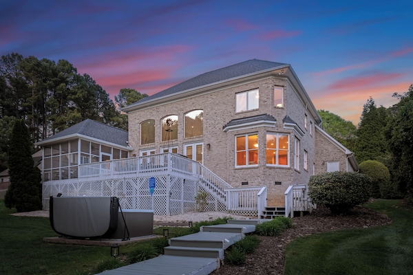 Beautiful brick home with a spacious deck, screened porch, and a glowing sunset backdrop.