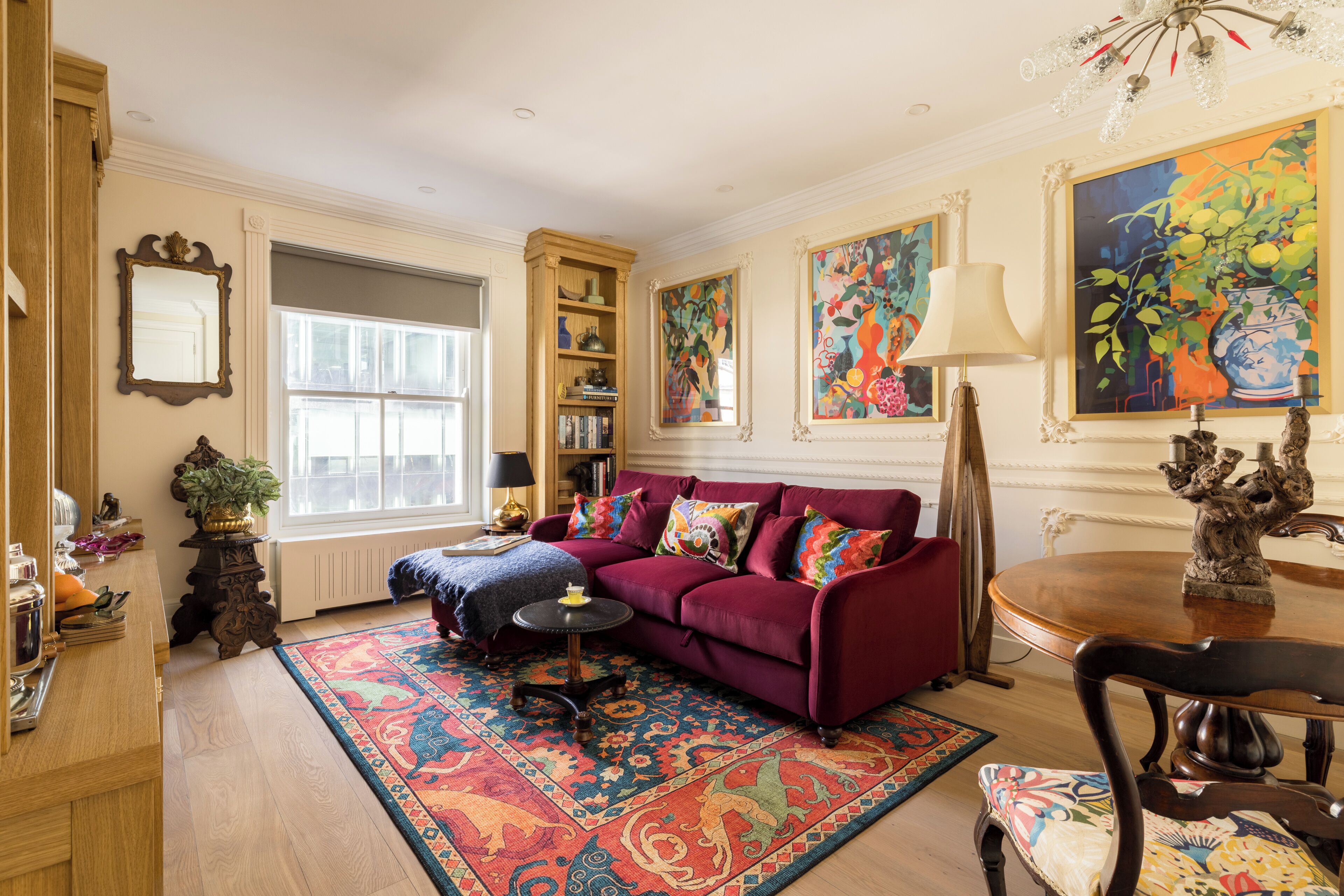 A living room with a red sofa, a patterned rug, a bookshelf, and a large window.