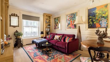 A living room with a red sofa, a patterned rug, a bookshelf, and a large window.