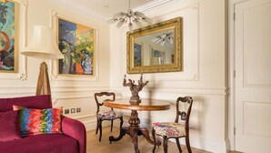 A room with a round wooden table, two chairs, a red sofa, a lamp, and a large mirror on the wall. - Paddington Station 2-Bed 4-Guest Designer Flat (London)