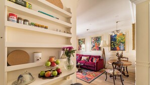 A living room with a sofa, a dining table with chairs, a vase with flowers, and shelves with various items. - Paddington Station 2-Bed 4-Guest Designer Flat (London)