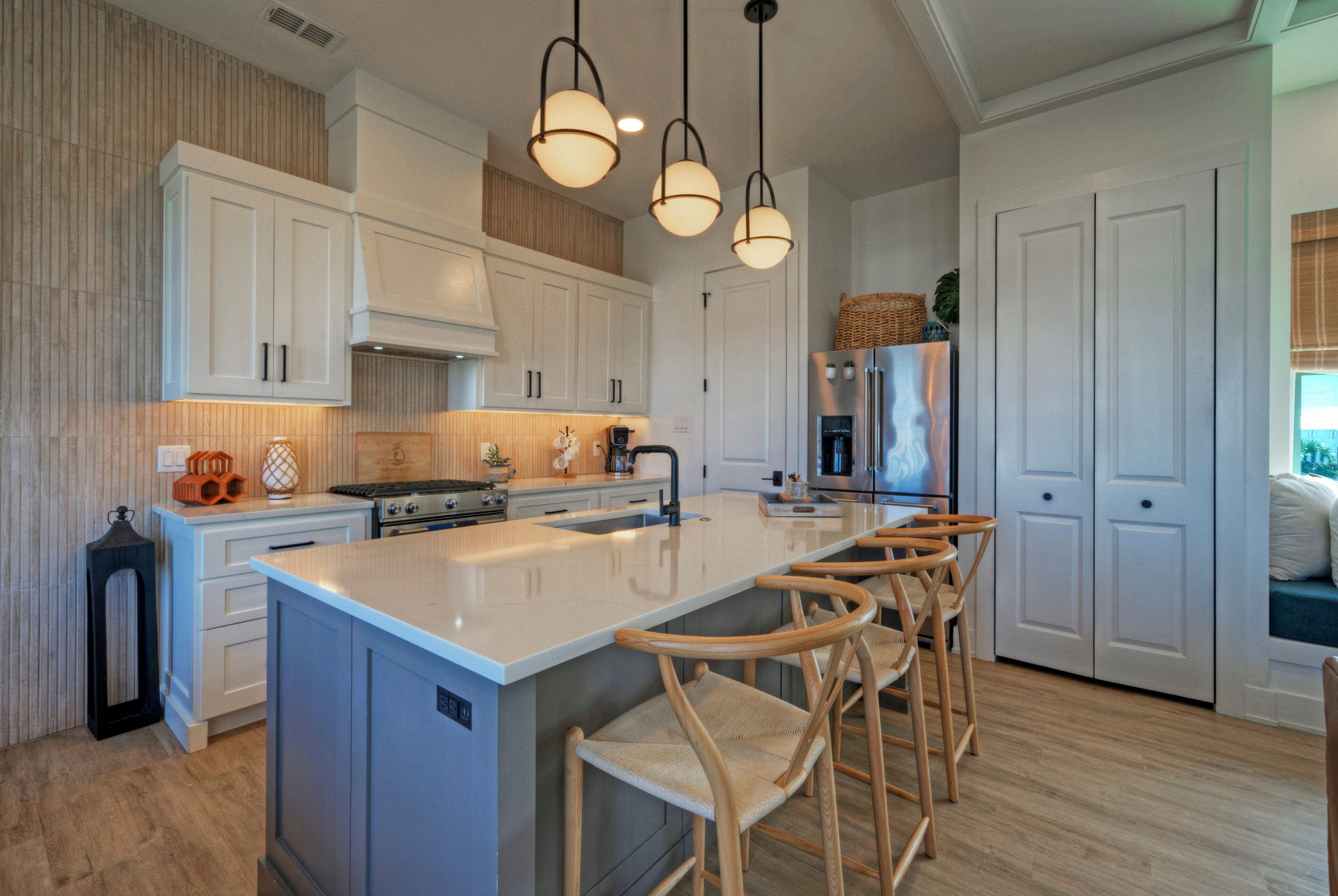 A modern kitchen with white cabinetry, a large island with bar stools, a stainless steel refrigerator, and pendant lighting.
