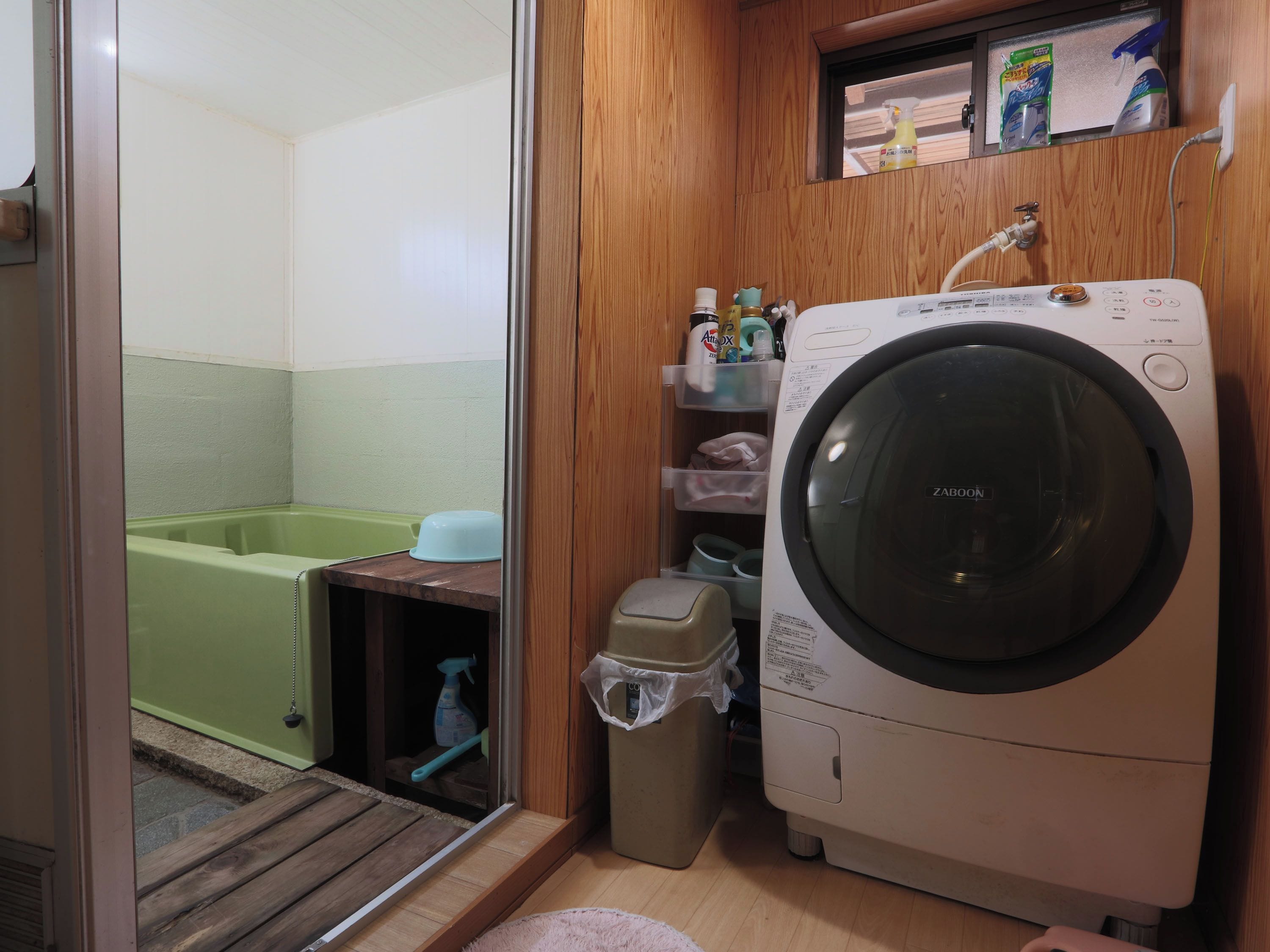 A compact laundry room with a washing machine, a green bathtub, and storage shelves.