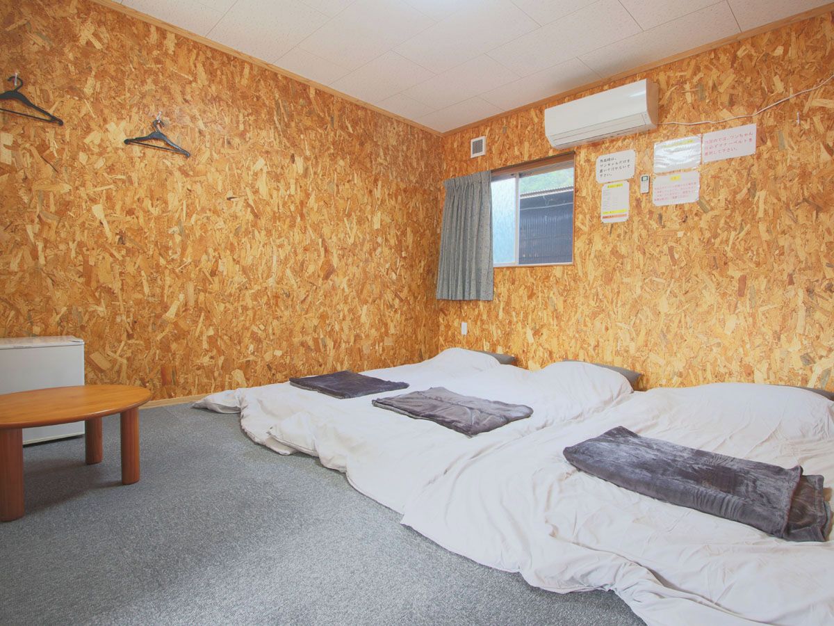 A room with a wooden wall, two beds, a table, and an air conditioning unit.