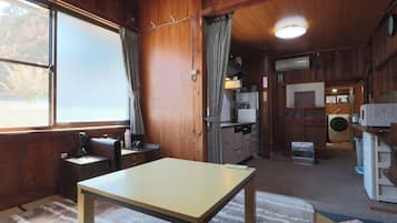 Interior de una cabaña con mesa de comedor, zona de cocina y un ventanal grande.