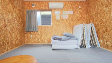 A room with a wooden wall, a window with curtains, a bed with pillows, a table, and an air conditioning unit.