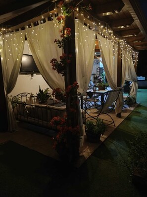 Eine Terrasse im Freien mit überdachter Sitzgelegenheit, Lichterketten und Blumentöpfen.