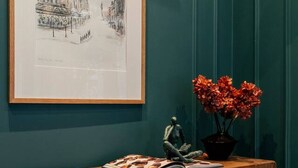 Een houten bank met daarboven een lijst met foto, een klein beeldje en een vaas met bloemen.