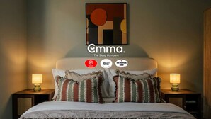 Een hotelkamer met een bed, twee nachtkastjes met lampen, een aan de muur hangend kunstwerk en drie badges met vermeldingen.
