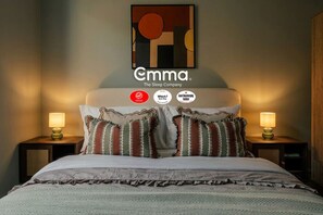 Ein Hotelzimmer mit einem Bett, zwei Nachttischen mit Lampen, einem Wandbild und drei Auszeichnungen.