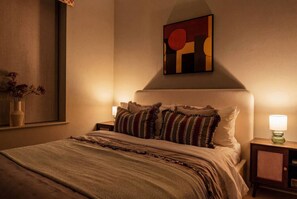 A bedroom with a bed, pillows, a nightstand, a lamp, a wall art piece, and a window with a vase. - Stunningly Designed Central 1-Bed Apartment (North Yorkshire)