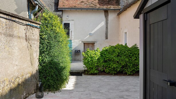 A narrow alleyway with a concrete path, a metal door, and a building with a tiled roof. - Gite de la Ferme de la Dalbeine – 25 min from Chenonceaux (Veuzain-sur-Loire)