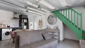 A living room with a sofa, a washing machine, a dining area, and a staircase. - Gite de la Ferme de la Dalbeine – 25 min from Chenonceaux (Veuzain-sur-Loire)