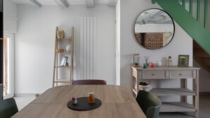 A dining area with a wooden table, chairs, a bookshelf, a desk with drawers, a mirror, and a staircase. - Gite de la Ferme de la Dalbeine – 25 min from Chenonceaux (Veuzain-sur-Loire)