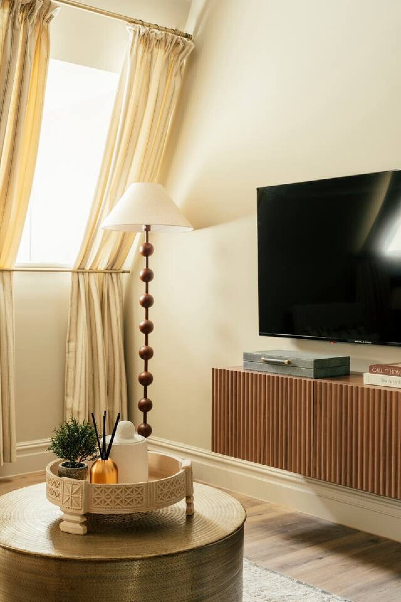 Een moderne woonkamer met een televisie, een lamp, een decoratietafel en een raam met gordijnen.