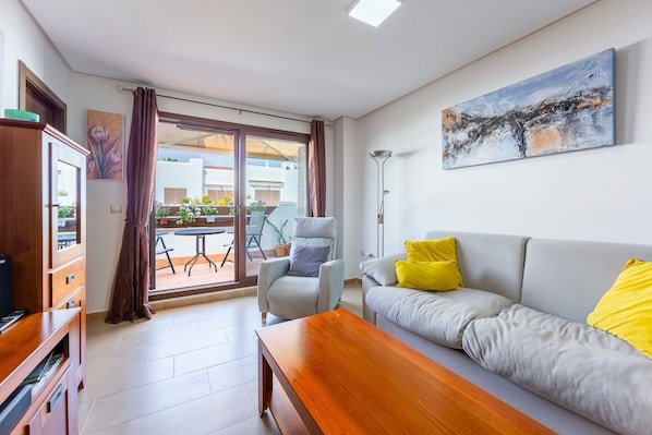 A modern living room with a sofa, armchair, wooden coffee table, and a painting on the wall.