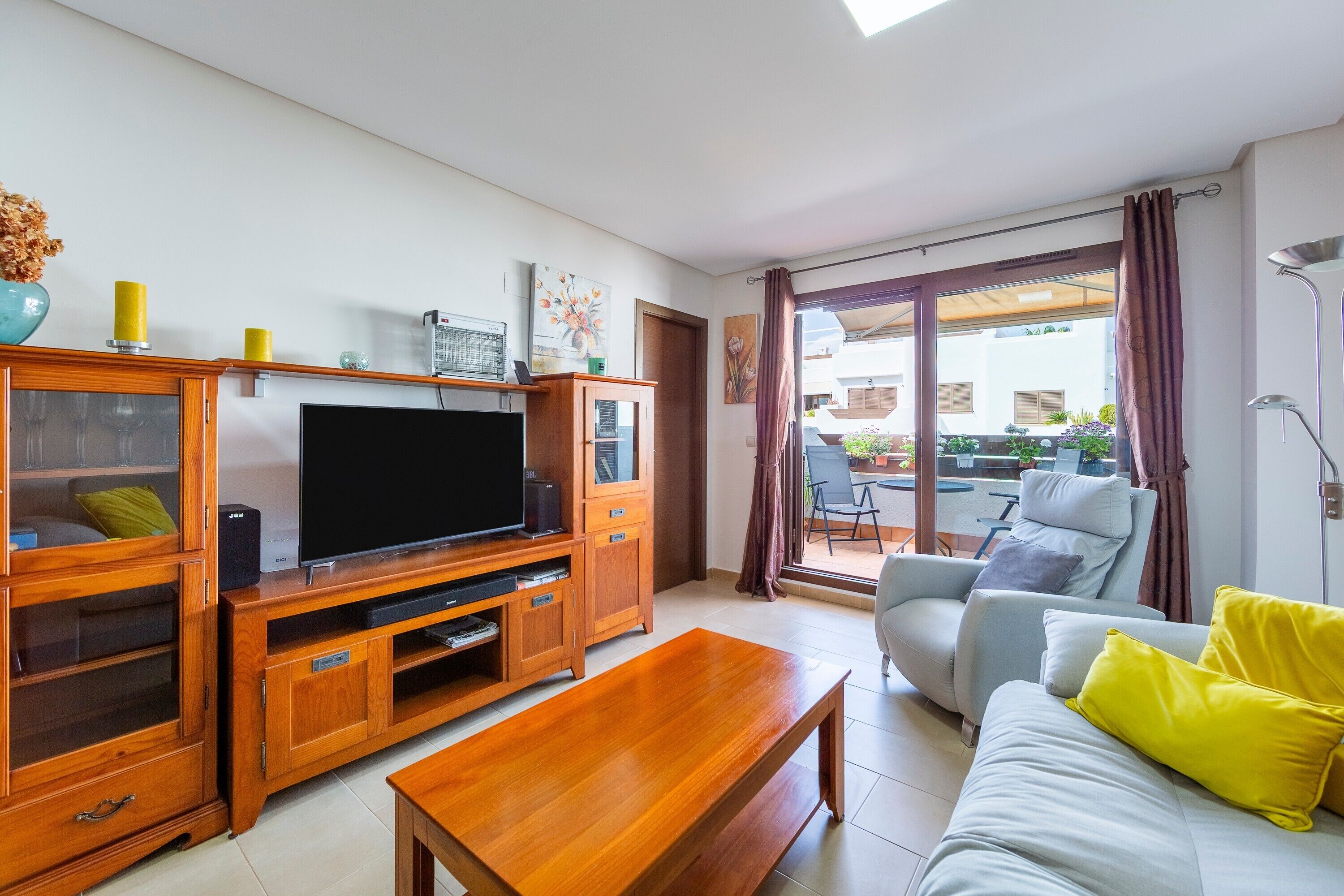 A living room with a TV, wooden entertainment unit, sofa, and a dining area with a table and chairs.