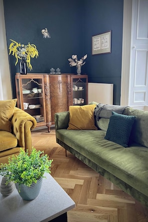 Una sala de estar con un sofá verde, un sillón amarillo, un aparador de madera y una planta en maceta.