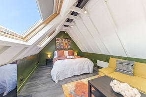 A bedroom with a skylight, a bed, a sofa, a colorful rug, and a wall art piece. - Stylish Harrogate Apartment (North Yorkshire)