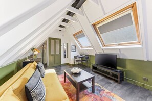 Ein Loftsesselzimmer mit hoher Decke, einer Couch, einem Fernseher und einem Essbereich.