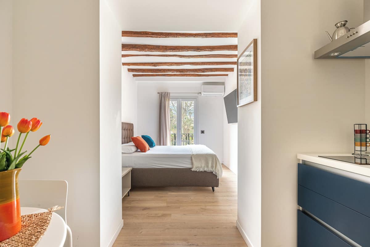 Quarto com cama, mesa de cabeceira, janela com cortinas e vista para o exterior.