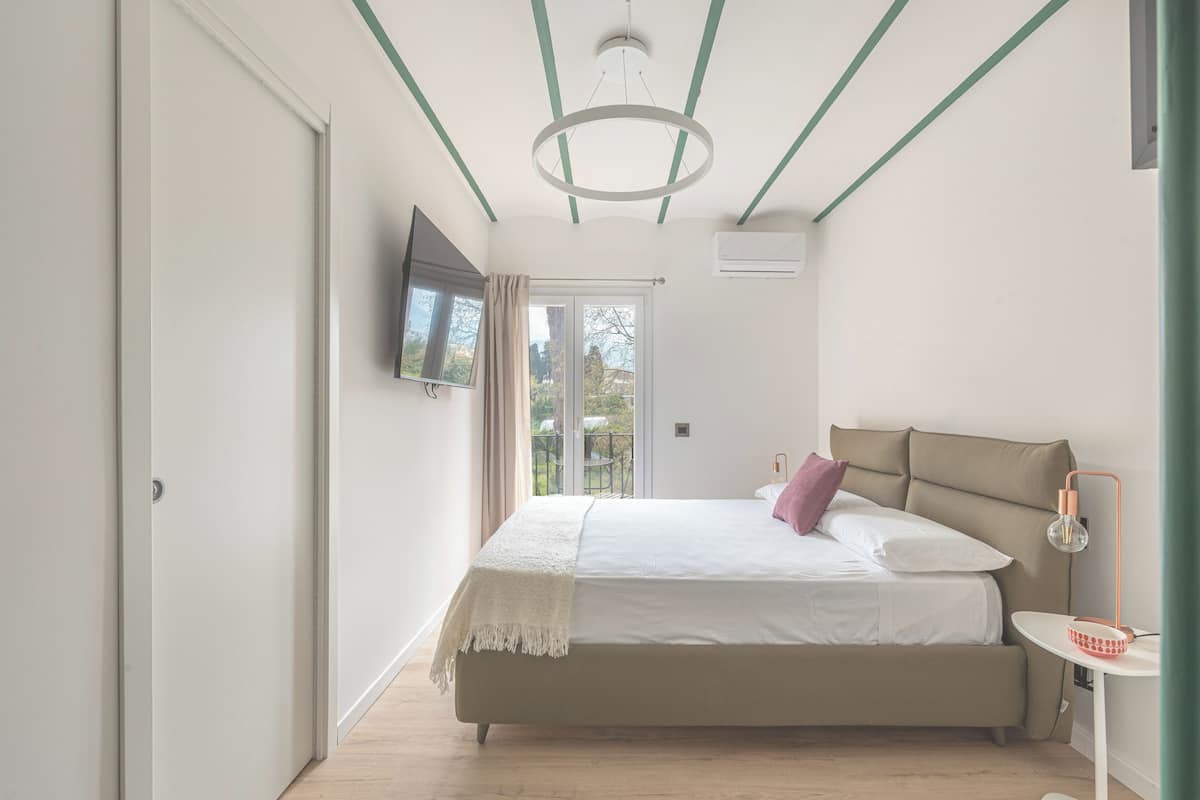 Quarto com cama, televisão, janela e luminária no teto.
