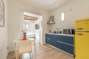 A compact kitchen with a yellow refrigerator, a microwave, and a stove. There is a dining area with a white table and chair. - Palazzo Ferrara Apartments with Balcony by Wonderful Italy (Palermo)