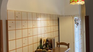 Un comedor con una mesa de madera, sillas, salpicadero de azulejos y una lámpara colgante.