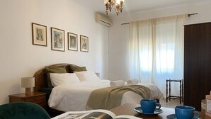 Habitación de hotel con cama, mesita de noche, una mesa de lectura con revistas y ventana con cortinas.