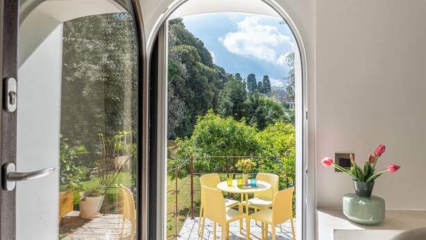 Un balcón con una mesa y sillas, una planta en maceta y vistas a un jardín exuberante.