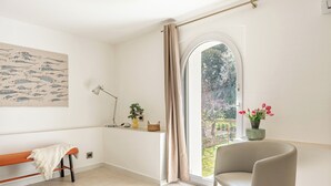 Una habitación con un banco, una silla, un ventanal con vistas, una lámpara y un papel tapiz decorado.