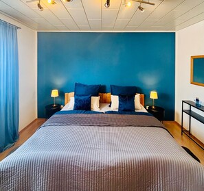 Ein Schlafzimmer mit einem großen Bett, zwei Nachttischen, einem Beistelltisch, einer blauen Wand und einer Decke mit Einbauleuchten.