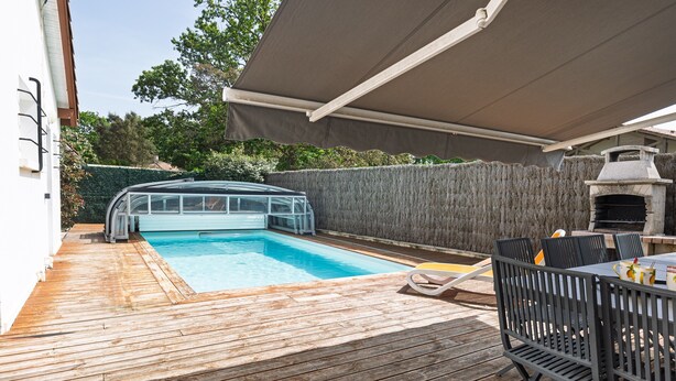 Un patio trasero con piscina, una parrilla y un porche cubierto.